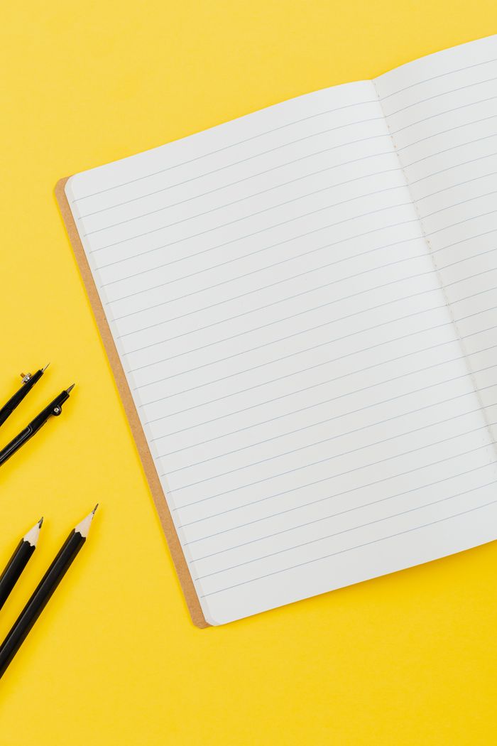 Flat lay of an open lined notebook with black pencils on a bright yellow background, offering ample copy space.