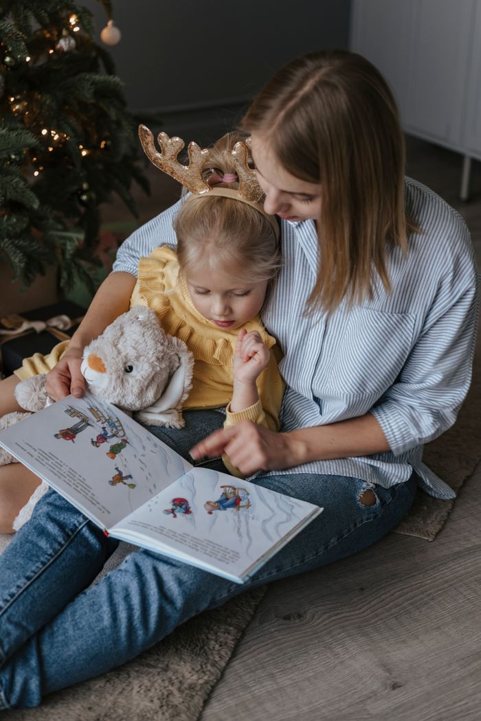 A mother and daughter bond while reading a book together with holiday decorations.