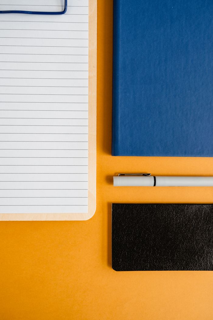 Flat lay of notepad, books, and pen on colorful background for office work.